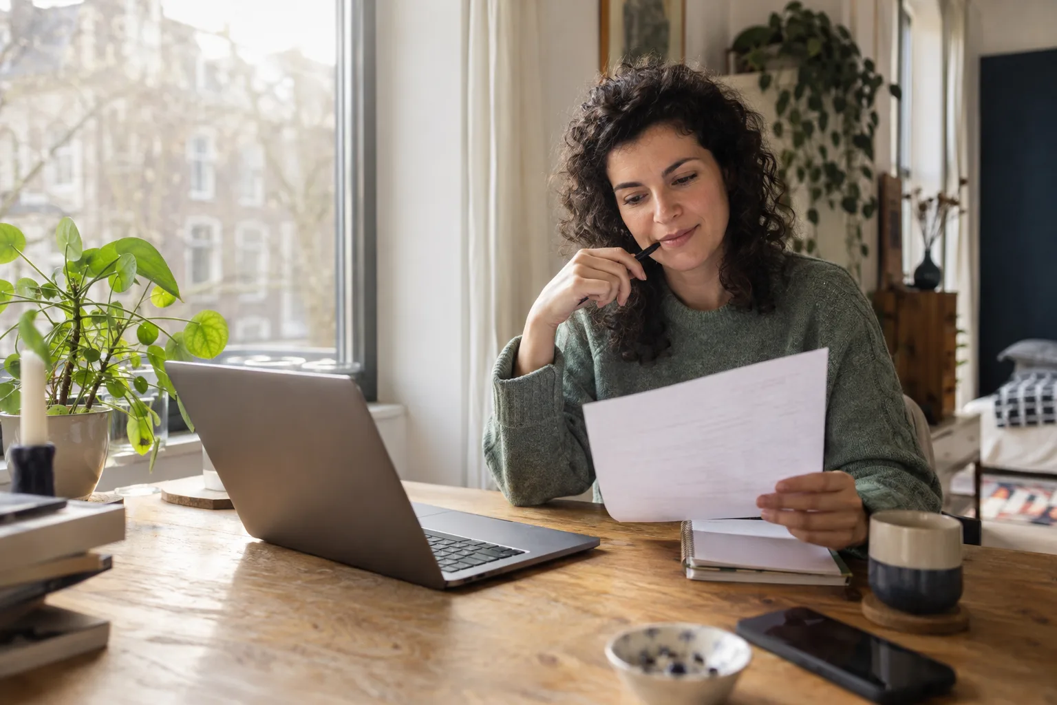 A woman reviews her CV at a desk by the window.